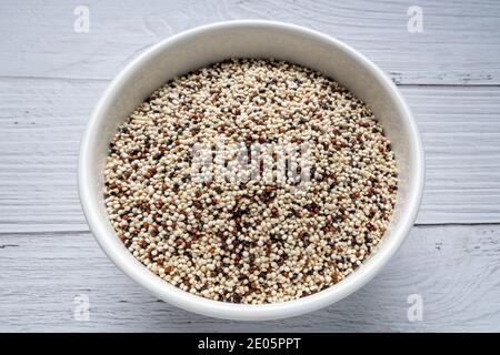 Mélange de quinoa cru dans un bol sur une table de cuisine en bois blanc. Vue de dessus. Aliments sains et diététiques super. Aliments végétaliens Banque D'Images