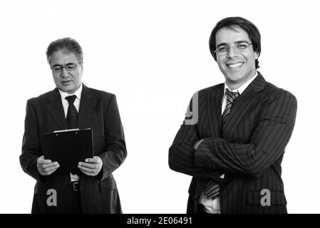 Les jeunes professionnels Persian businessman smiling with arms crossed et senior businessman reading perse sur presse-papiers Banque D'Images