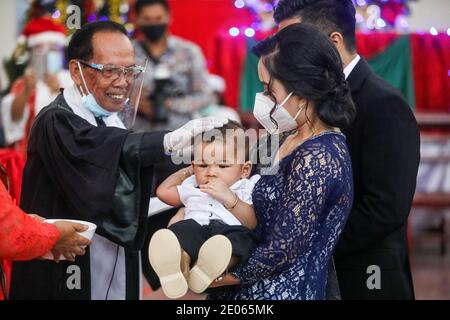 Un prêtre portant un bouclier facial comme mesure contre la propagation de Covid19 est vu poser sa main sur un tout-petit pendant la cérémonie de baptême des enfants de congrégation chrétienne à l'église protestante Batak Karo à Medan. Banque D'Images