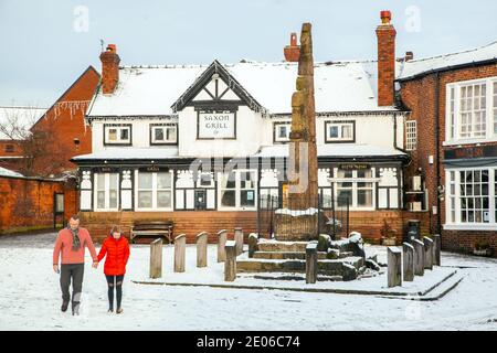 Les gens qui marchent devant les croix de pierre de l'ancienne Saxe dans le La neige pavée couvrait la place du marché en hiver à Sandbach Cheshire Angleterre Banque D'Images