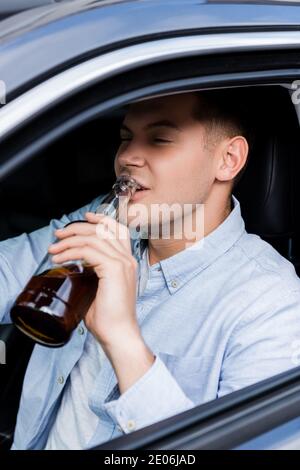 un jeune homme boit du whisky tout en conduisant une voiture sur un premier plan flou Banque D'Images