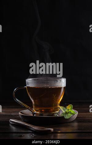 Infusion de menthe poivrée à la vapeur dans un verre de cristal avec des feuilles de menthe fraîche, sur une base en bois rustique sombre. Banque D'Images