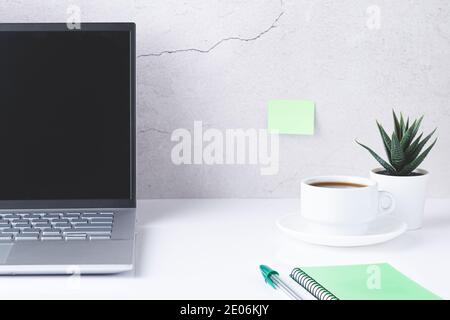 Bureau blanc avec ordinateur portable, tasse de café, carnet vert et stylo. Banque D'Images