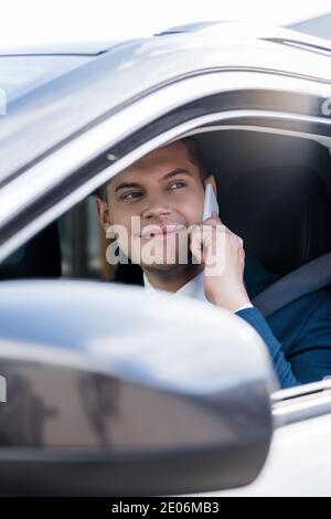 Homme d'affaires souriant parlant automatiquement sur smartphone au premier plan flou Banque D'Images