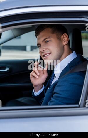 Homme d'affaires souriant en tenue habillée parlant sur smartphone en voiture Banque D'Images