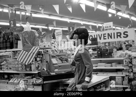 Jeune femme afro-américaine agitant le drapeau Stars and Stripes elle travaille dans un grand magasin du centre ville de Manhattan New York 1972. ANNÉES 1970 USA HOMER SYKES Banque D'Images