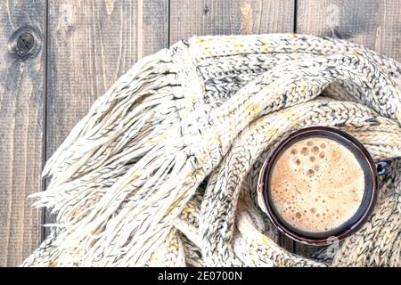 Tasse de café chaud avec mousse sur fond de table rustique en bois enveloppé d'un foulard en laine de tricot chaud. Tasse de cappuccino. Concept d'hiver, chaleur, holida Banque D'Images