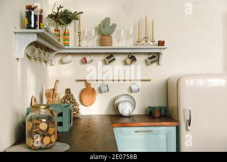 Maison rustique cuisine intérieur: comptoir en bois avec réfrigérateur rétro, étagères avec tasses et ustensiles, couleurs pastel. Banque D'Images