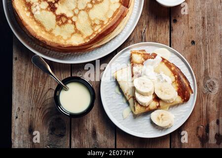 Crêpes fines, crêpes aux bananes et lait condensé dans une assiette sur une table en bois. Banque D'Images