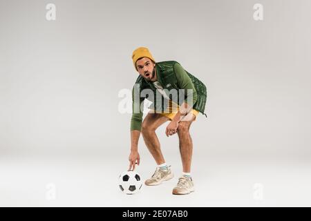 Homme choqué regardant la caméra près du football sur fond gris Banque D'Images