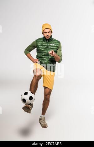 Un sportif sérieux se dirige avec le doigt vers l'appareil photo tout en jouant au football sur fond blanc Banque D'Images