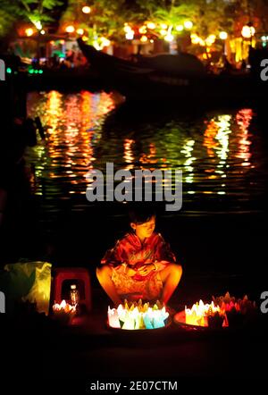 Fille vendant des lanternes en papier au festival de pleine lune à Hoi an, Vietnam avec des lumières reflétées dans la rivière Banque D'Images