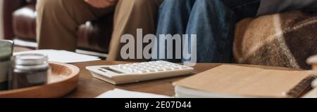 vue rognée d'un couple âgé assis près d'une table avec calculatrice blanche à la maison sur fond flou, bannière Banque D'Images