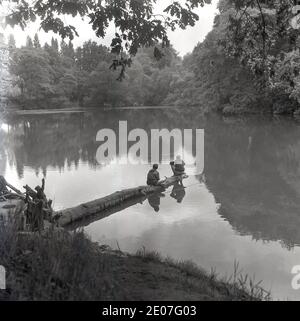 Années 1950, historique, deux jeunes garçons au bout d'un arbre tombé au milieu d'un lac, Angleterre, Royaume-Uni. Banque D'Images