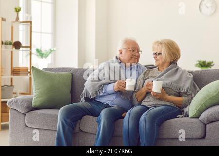 Couple d'âge mûr souriant grands-parents assis ensemble sur le canapé et réchauffant avec du thé chaud Banque D'Images