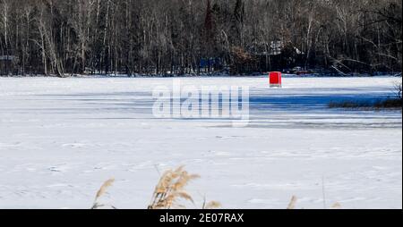 Petite pêche de glace rouge de la manty sur le lac gelé avec neige et ciel bleu Banque D'Images