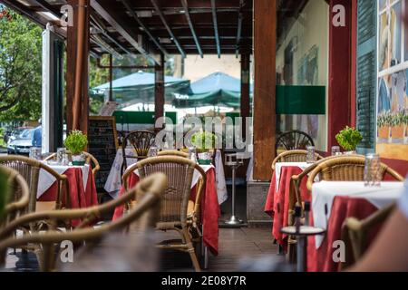 Balcon vide avec tables prêtes à recevoir les invités pour le déjeuner, avec des rideaux rouges et des chaises en osier dans une journée ensoleillée à Madère, portugal Banque D'Images