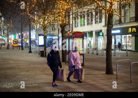 Manchester, Angleterre, Royaume-Uni. 30 décembre 2020. Scènes des environs du centre-ville de Manchester tard le soir du 30. À minuit, la ville sera placée sous les restrictions de niveau 4 du coronavirus après une annonce du gouvernement plus tôt aujourd'hui. Deux femmes portant un masque facial marchent dans la rue en portant des sacs à provisions. Crédit : Callum Fraser/Alay Live News Banque D'Images