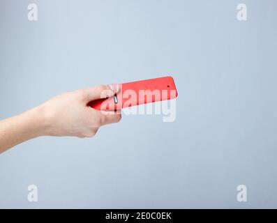 La main femelle tient la télécommande du téléviseur dans un étui en silicone rouge sur fond gris Banque D'Images