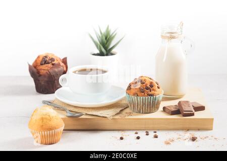 Une variété de muffins avec une tasse de chocolat au lait sur une planche de bois sur fond blanc. Banque D'Images