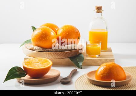 Oranges, tranches d'oranges, feuilles d'orange et récipients en verre avec jus d'orange sur fond blanc. Banque D'Images