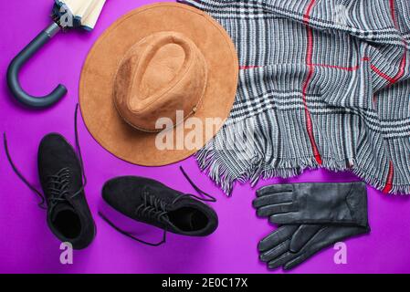 Chaussures et accessoires tendance pour femme sur fond violet. Bottes noires, chapeau en feutre, gants en cuir, parapluie. Vue de dessus Banque D'Images