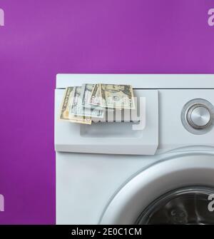 Billets de dollars dans le lave-linge sur fond violet. Concept de lavage coûteux Banque D'Images