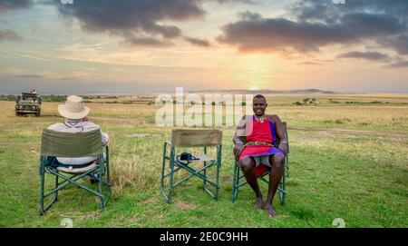 Réserve nationale de Maasai Mara, Kenya - 29 septembre 2013. Un guide de safari kenyan et un invité américain se détendent lors d'une pause-détente en voiture au coucher du soleil. Banque D'Images