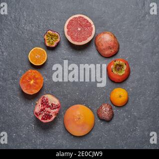 Vue de dessus de l'orange, du pamplemousse, de la grenaille, des fruits de la passion et du kaki sur fond de pierre gris foncé disposés en cercle. Fruits frais et sains Banque D'Images