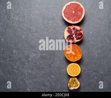 Vue de dessus de l'orange, du pamplemousse, de la grenaille, des fruits de la passion et du kaki sur fond de pierre gris foncé disposé en ligne. Fruits frais et sains Banque D'Images