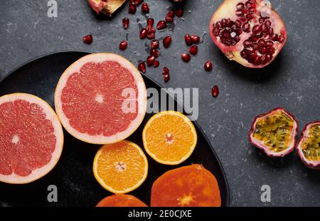 Gros plan d'orange, de pamplemousse, de grengrade, de fruit de la passion et de kaki sur fond de pierre gris foncé. Fruits frais et sains pour stimuler la vitamine C. Banque D'Images