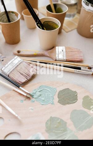 Vue de dessus de la palette de bois avec peintures vert pastel et brosses professionnelles sur table en atelier Banque D'Images