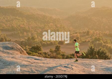 Vue latérale d'un coureur mâle mince qui court sur les rochers montagnes au coucher du soleil en soirée pendant l'entraînement actif Banque D'Images