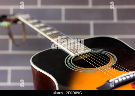 Guitare acoustique noire et orange sur fond de mur de briques. Concentrez-vous sur le trou et les cordes sonores. Industrie de la musique, concepts d'affaires de divertissement Banque D'Images