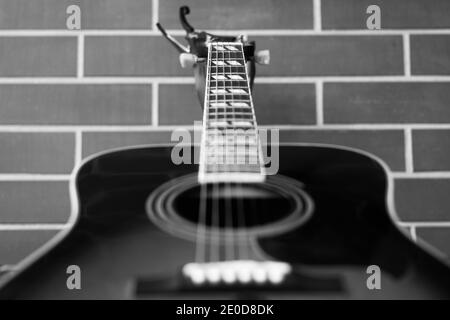 Guitare acoustique gros plan sur fond de mur de briques. Concentrez-vous sur le trou et les cordes sonores. Photographie en noir et blanc Banque D'Images