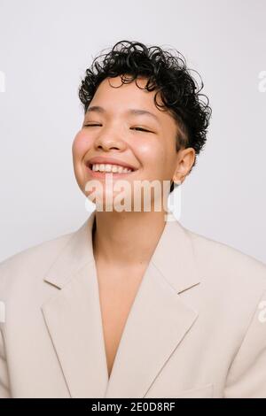 Jeune femme Latina avec les yeux asiatiques souriant et portant un blazer beige, photo verticale isolée, fond blanc Banque D'Images