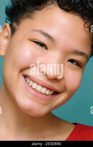 Portrait de la jeune femme Latina avec les yeux asiatiques regardant l'appareil photo et souriant, gros plan, photo verticale isolée, arrière-plan vert tidewater Banque D'Images