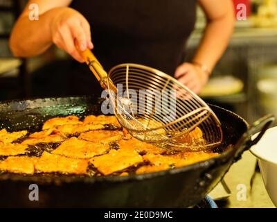 Faites frire des morceaux de pâte à frire de louches métalliques à un chef méconnaissable dans une casserole avec de l'huile chaude tout en travaillant dans une cuisine professionnelle Banque D'Images