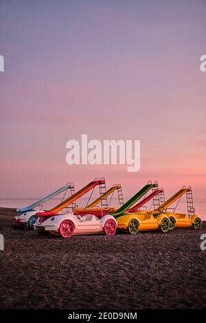 Collection de pédalos colorés avec toboggans placés sur du sable plage sur fond de coucher de soleil rose sur la mer en Espagne Banque D'Images