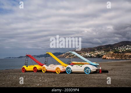 Collection de pédalos colorés avec toboggans placés sur du sable plage sur fond de coucher de soleil rose sur la mer en Espagne Banque D'Images