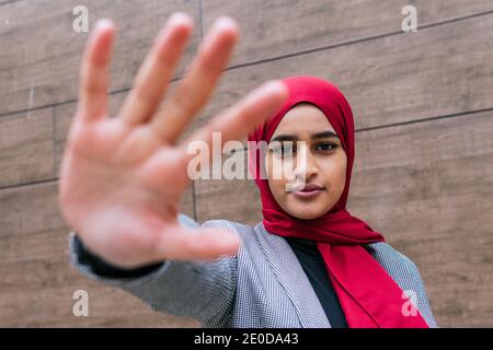 Angle bas de la gaie arabe femme dans hijab regardant appareil photo et réaliser des gestes avec les mains en étant debout dans la rue Banque D'Images