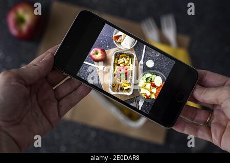De dessus de la récolte blogueur méconnaissable prenant la photo de choses à emporter nourriture préparée pour le déjeuner tout en utilisant un smartphone Banque D'Images