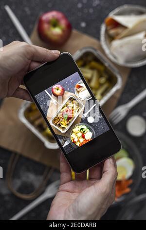 De dessus de la récolte blogueur méconnaissable prenant la photo de choses à emporter nourriture préparée pour le déjeuner tout en utilisant un smartphone Banque D'Images