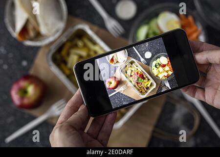 De dessus de la récolte blogueur méconnaissable prenant la photo de choses à emporter nourriture préparée pour le déjeuner tout en utilisant un smartphone Banque D'Images