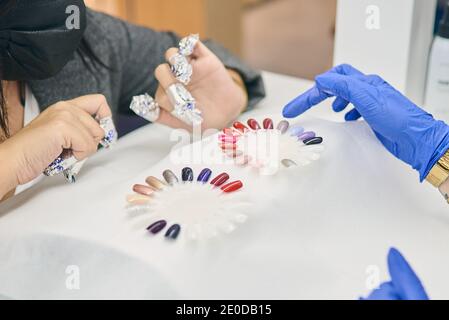 Crop anonyme femme choisissant la couleur de la palette de vernis à ongles tout en étant assis à table avec maître de manucure dans le salon de beauté moderne Banque D'Images