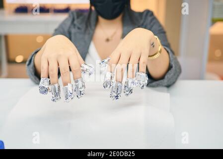 Client de culture féminine méconnaissable assis à la table dans un salon de manucure et le gel nettoyant à l'aide d'un film Banque D'Images