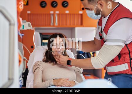 Rognez le masque du ventilateur de pose d'un paramédical masculin sur le patient allongé civière médicale dans une voiture d'ambulance Banque D'Images