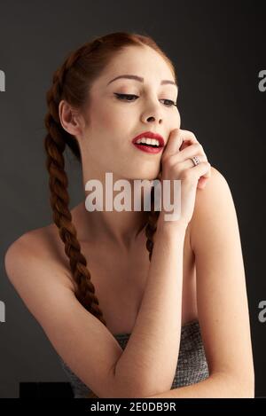 Modèle féminin élégant avec cheveux rouges et tresses studio sur fond sombre et vue sur l'extérieur Banque D'Images