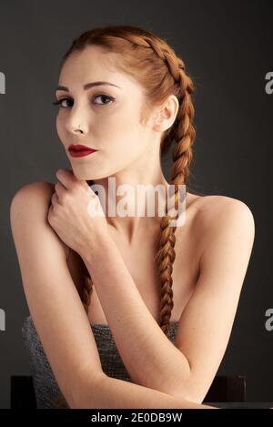 Modèle féminin élégant avec cheveux rouges et tresses studio sur fond sombre et regardant l'appareil photo Banque D'Images