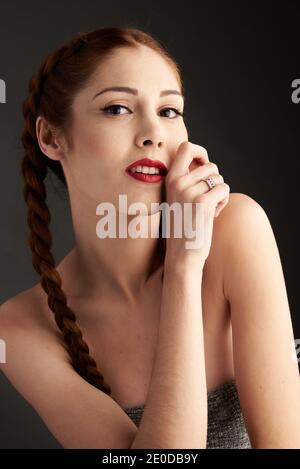 Modèle féminin élégant avec cheveux rouges et tresses studio sur fond sombre et regardant l'appareil photo Banque D'Images